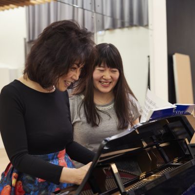 Teacher and student standing at a piano and smiling